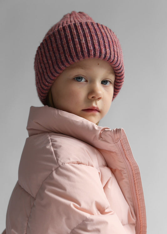 Child wearing the Belacaro kids beanie in heather pink baby alpaca, styled with a soft pink puffer jacket, side portrait view.