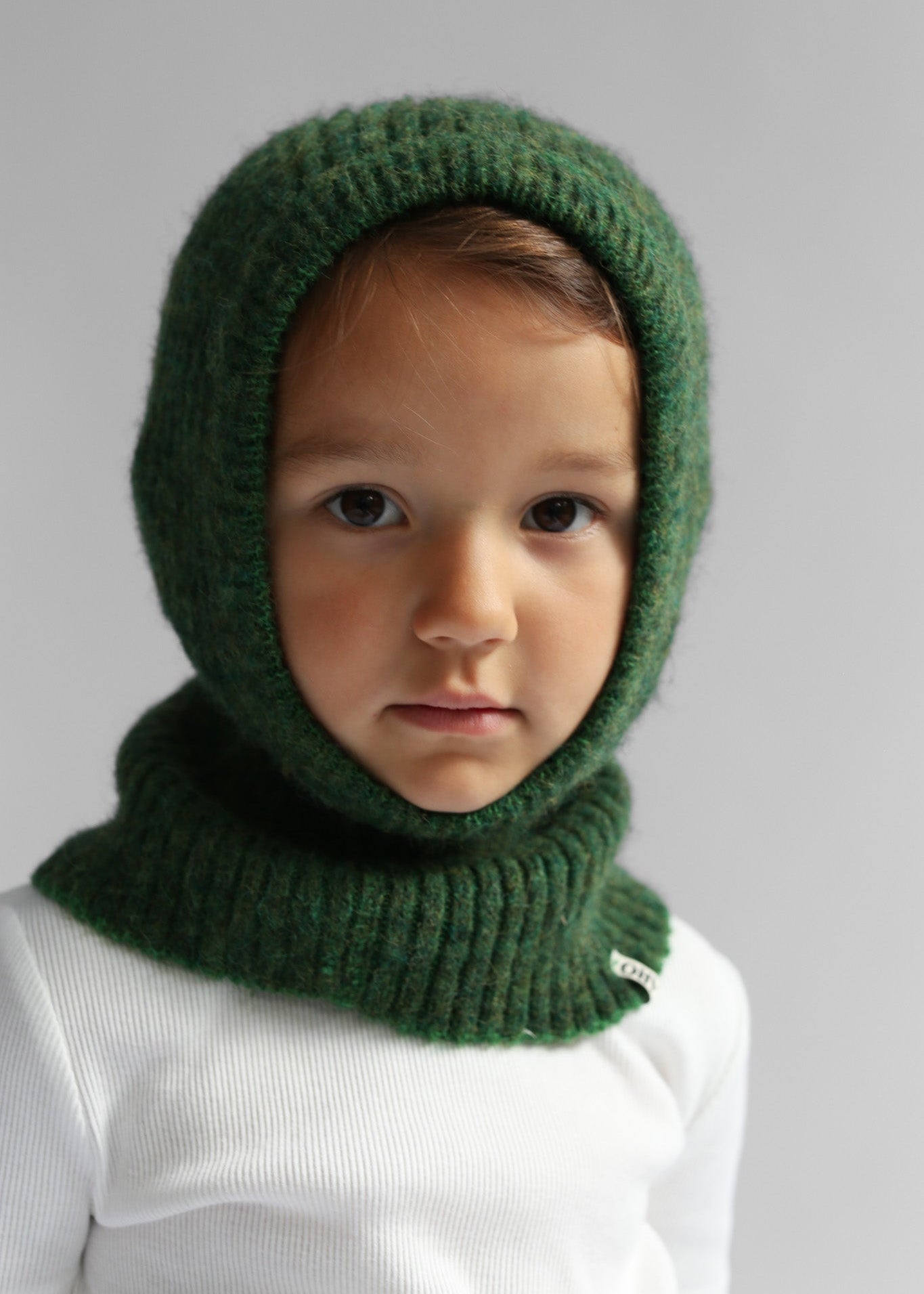 Portrait of a kid wearing a green balaclava against a white background