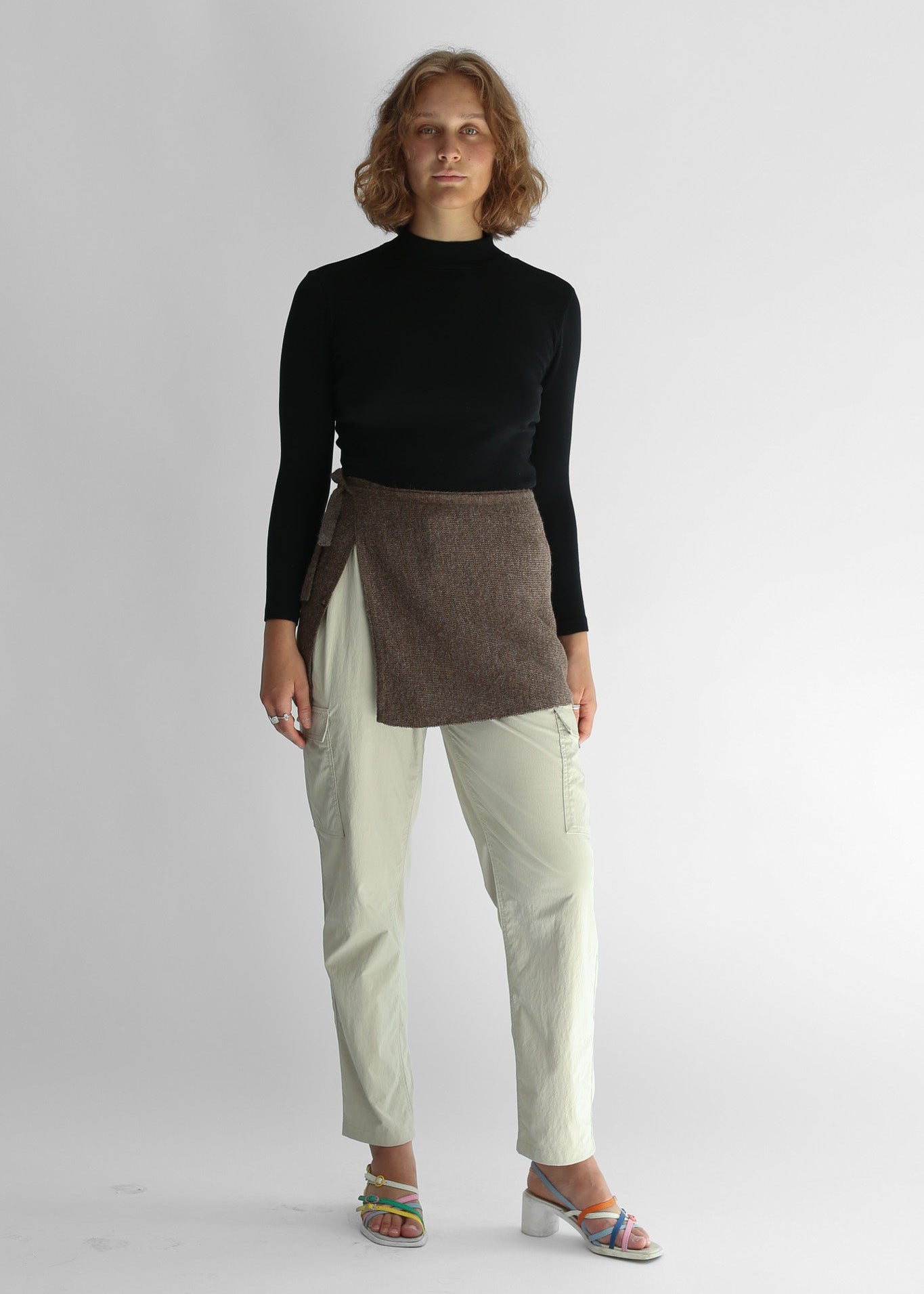 A woman wearing a brown knit skirt over white pants and black sweater
