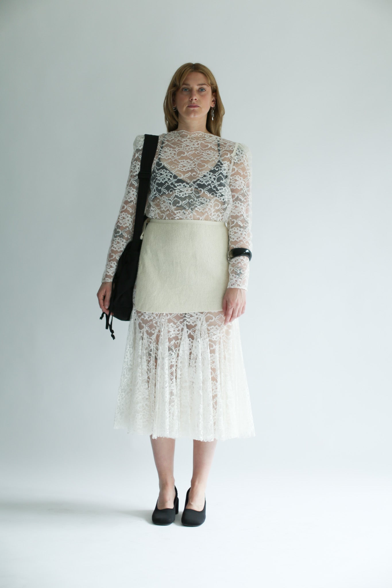 Woman wearing a white knit skirt over a lace dress with a plain background