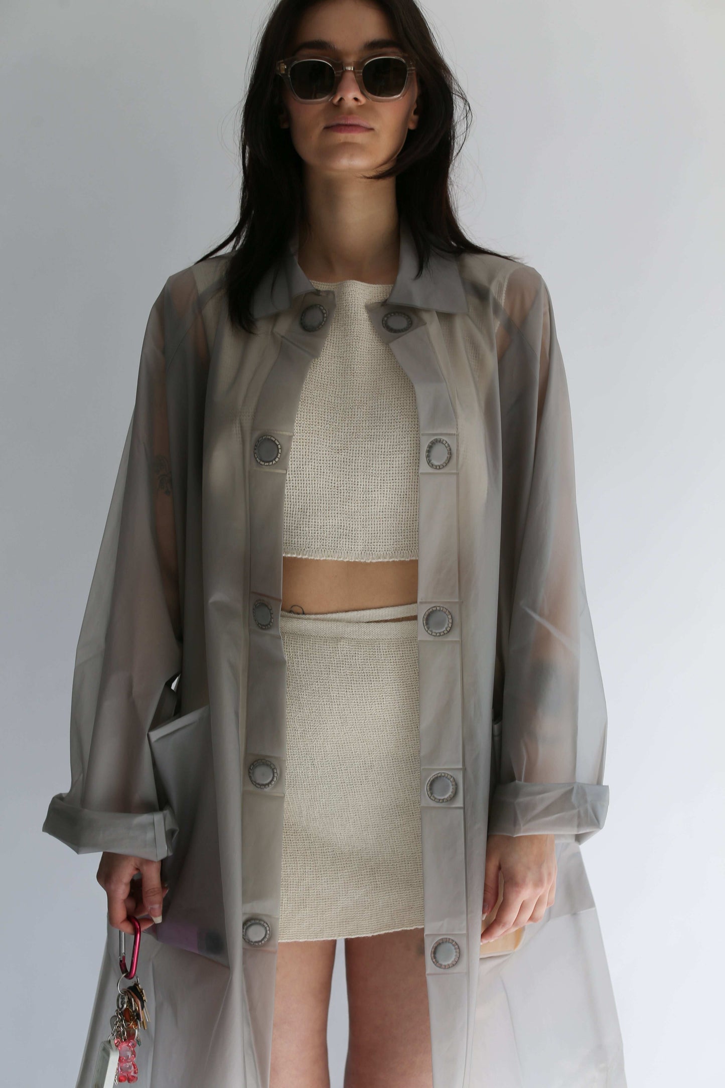 Woman wearing a transparent trench coat over a white knit croptop and white knit skirt