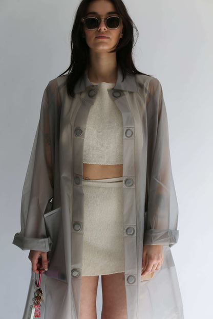Woman wearing a transparent trench coat over a white knit croptop and white knit skirt
