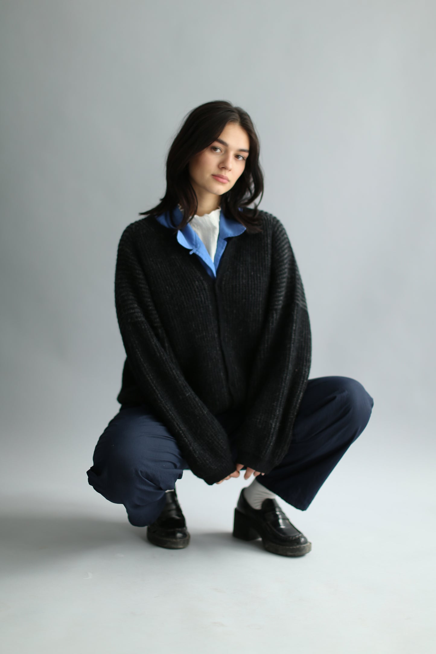 A model wearing a grey and black ribbed cardigan and navy pants with black loafers