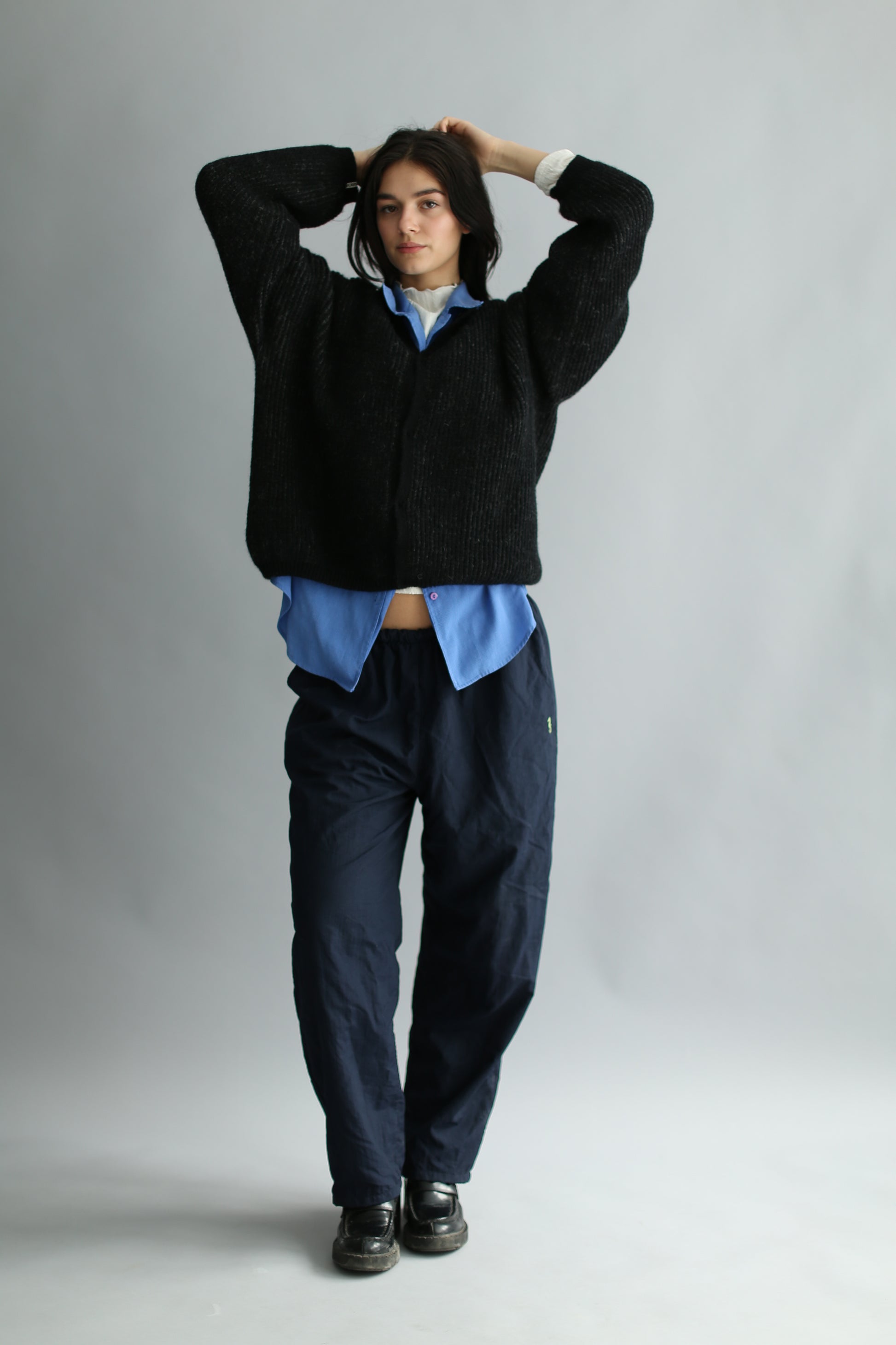 A model wearing a grey and black ribbed cardigan, navy pants, black loafers