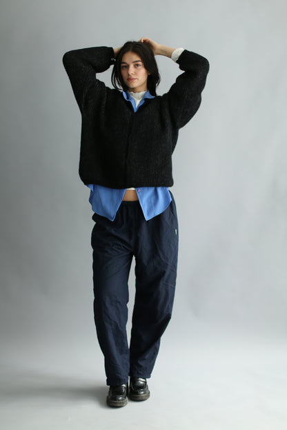 A model wearing a grey and black ribbed cardigan, navy pants, black loafers