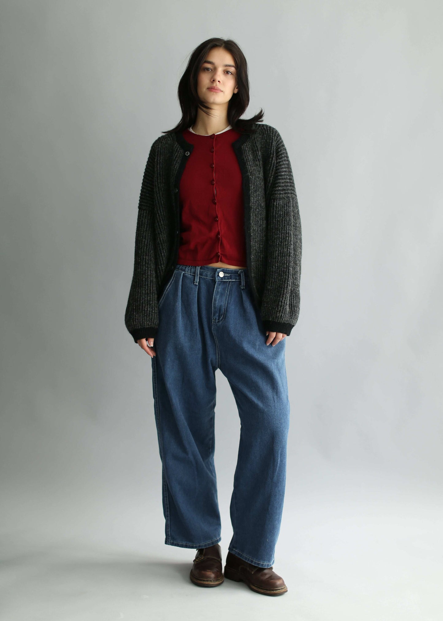 Portrait of a model wearing a grey and black ribbed cardigan with red knit and blue jeans