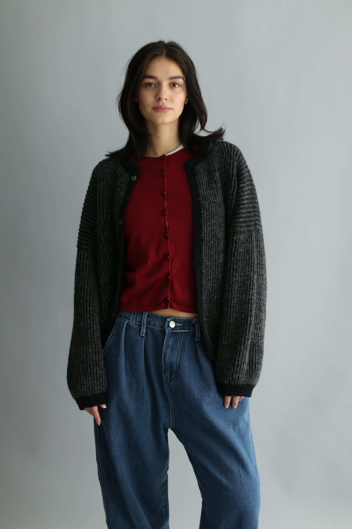 Portrait of a model wearing a grey and black ribbed cardigan with red knit and blue jeans