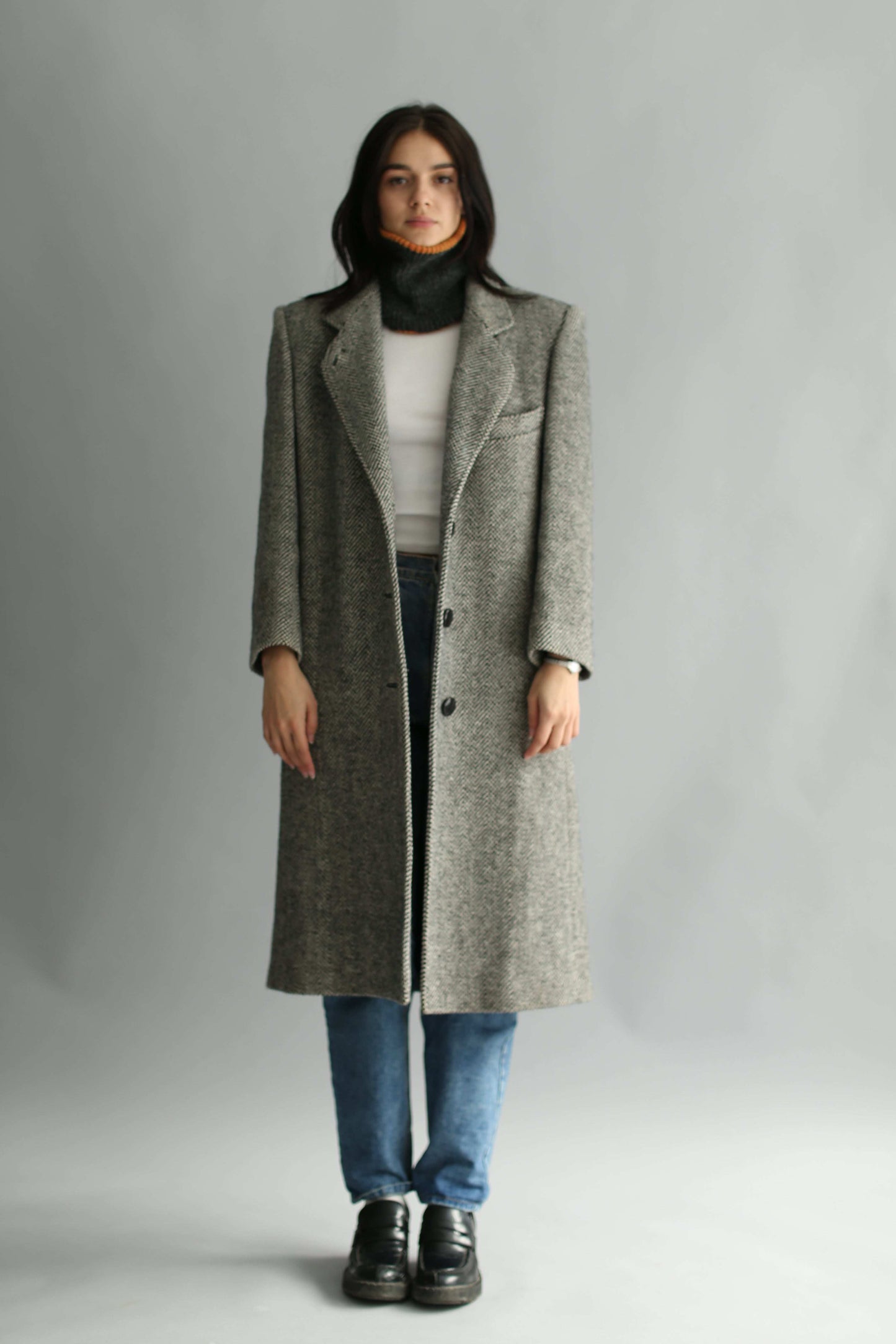 Woman wearing a black neck warmer, a tweed grey coat and white sweater on a white background