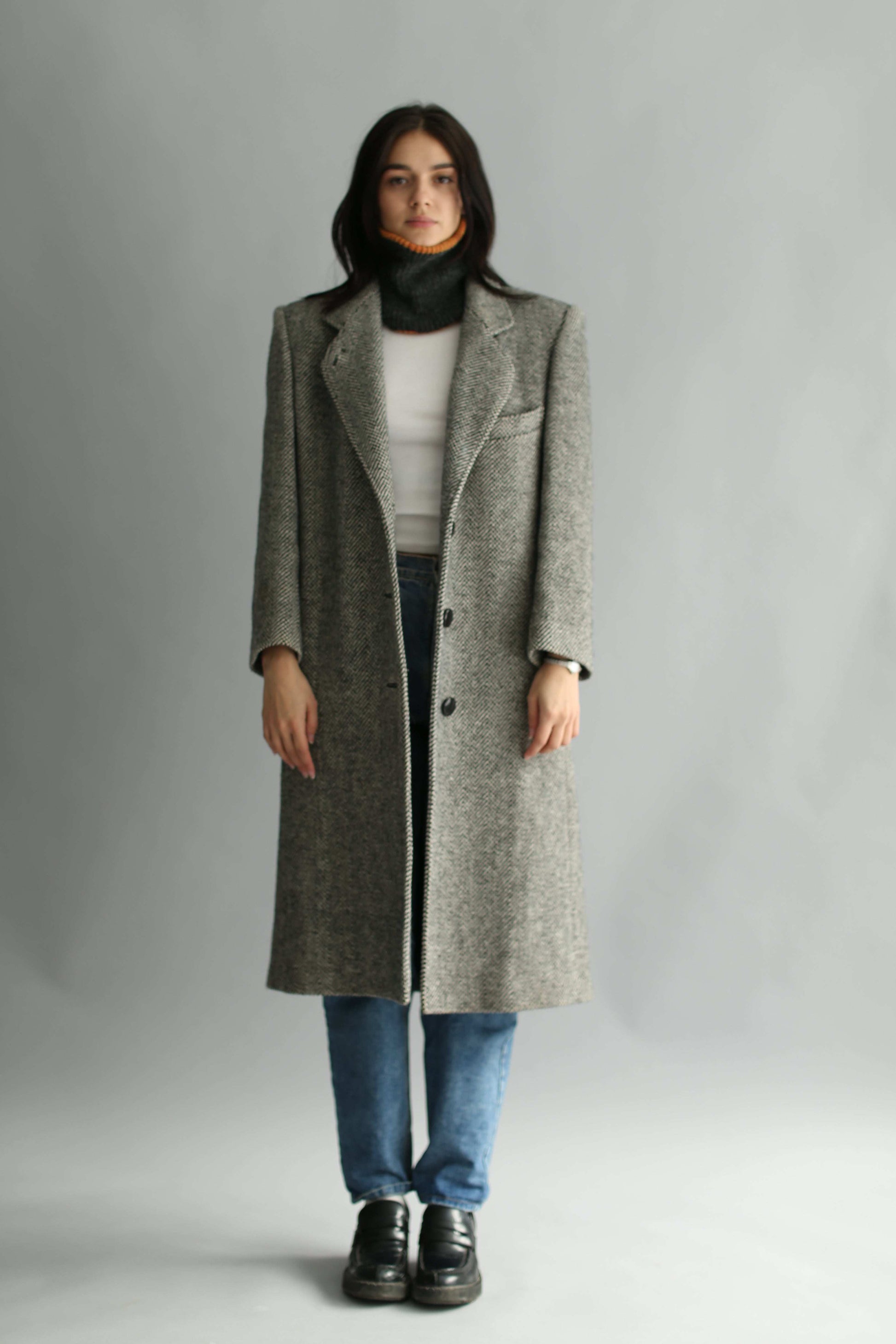 Woman wearing a black neck warmer, a tweed grey coat and white sweater on a white background