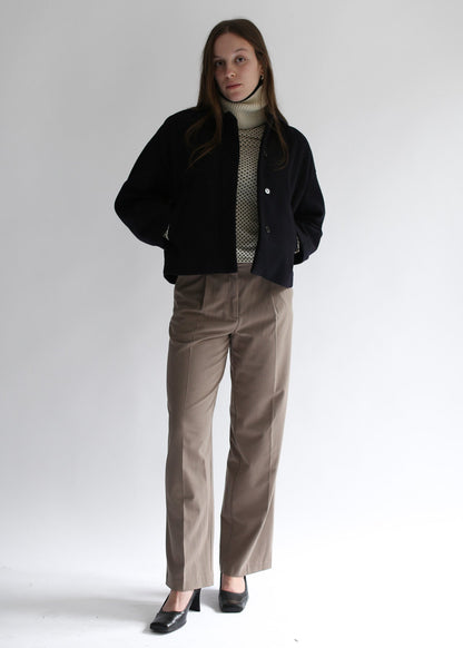 Model wearing a white neck warmer, a black jacket, beige sweater, and brown pants on a white background