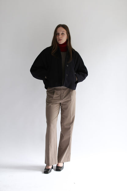 Model wearing a white neck warmer, a black jacket and brown pants on a white background