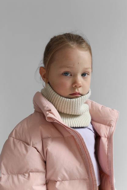 Child wearing a pink puffer jacket and white neck warmer against a plain background