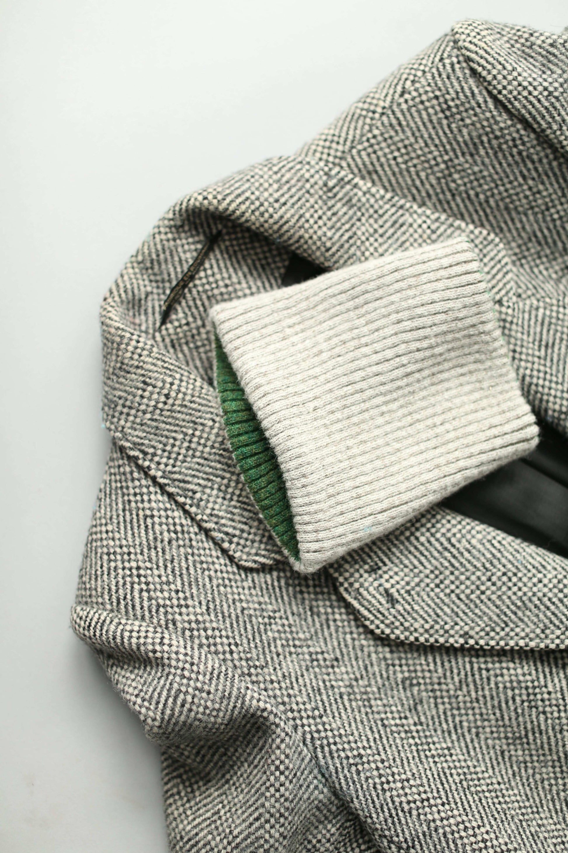 A white and green neck warmer on a grey herringbone coat