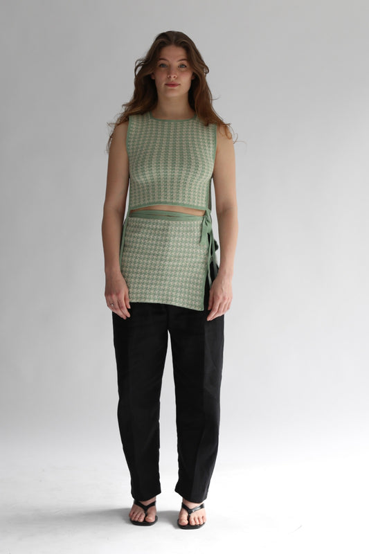 Woman wearing a green houndtooth top and black pants on a white background