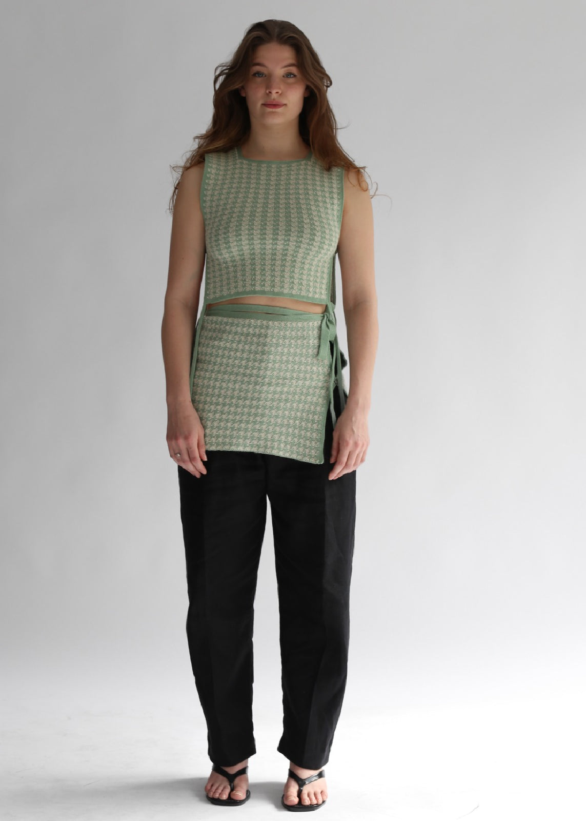 Woman wearing a green houndtooth top and black pants on a white background