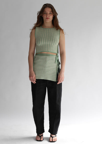 Woman wearing a green houndtooth top and black pants on a white background