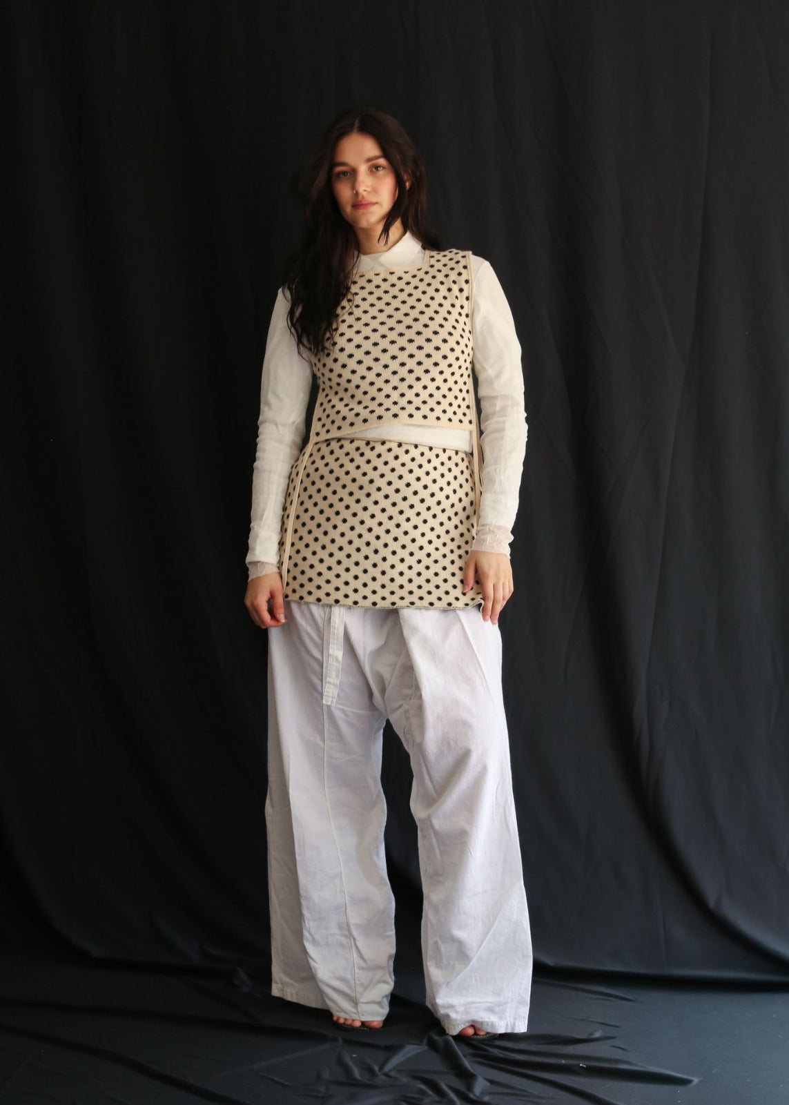 Woman wearing a white polka dot top and skirt on a dark background