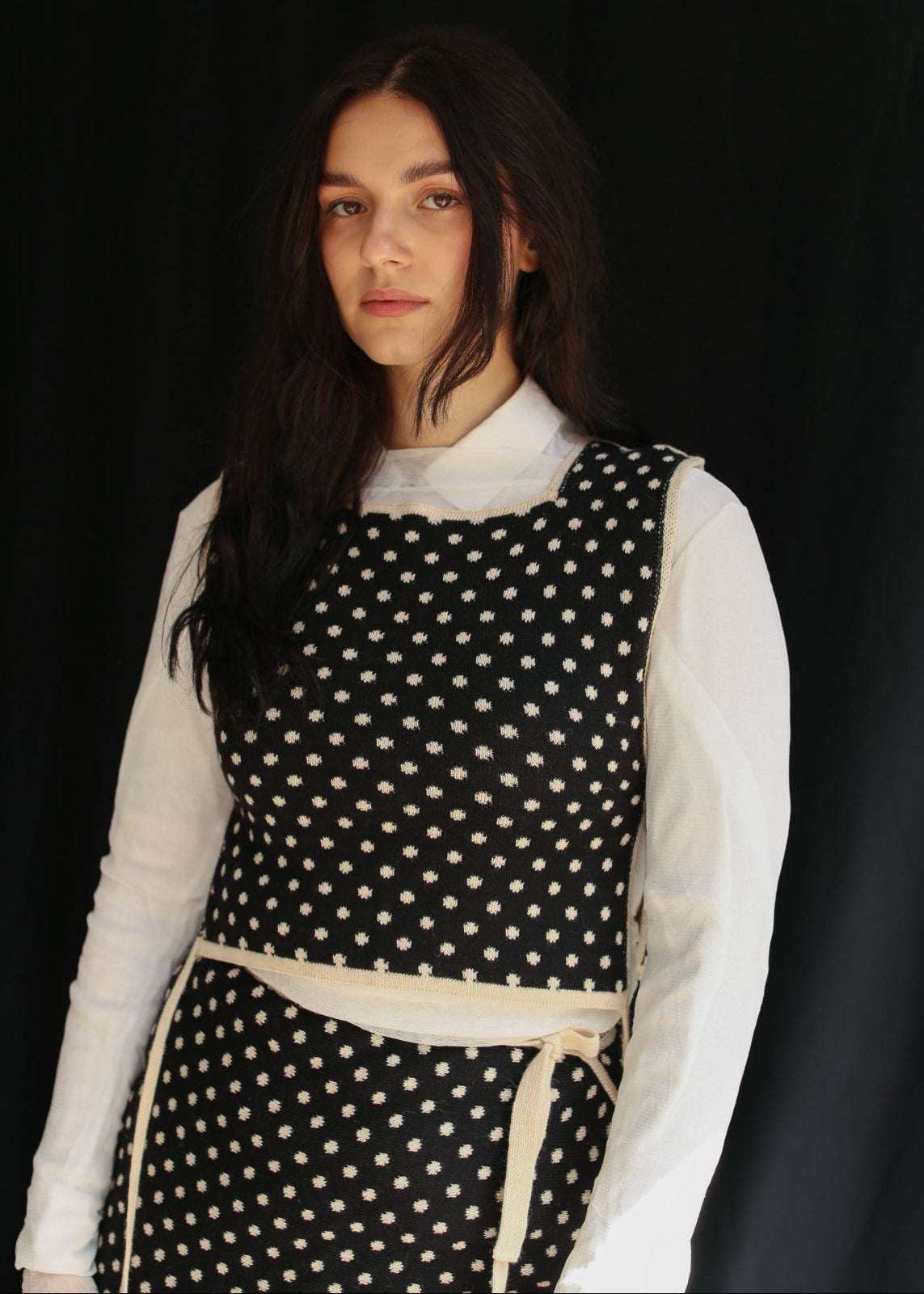 Woman wearing a knitted top and skirt, polka dot patterned in front of a dark background