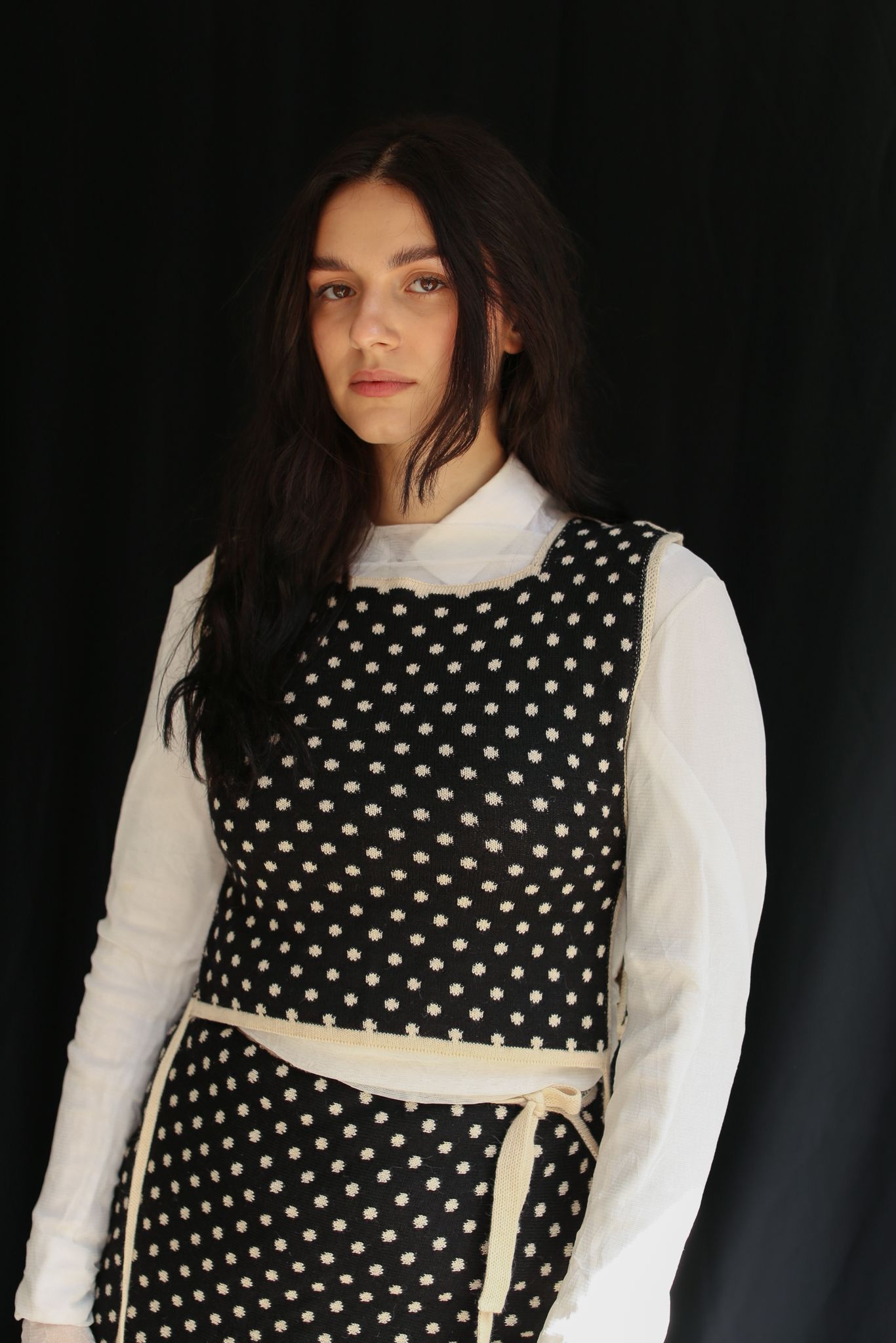 Woman wearing a knitted top and skirt, polka dot patterned in front of a dark background