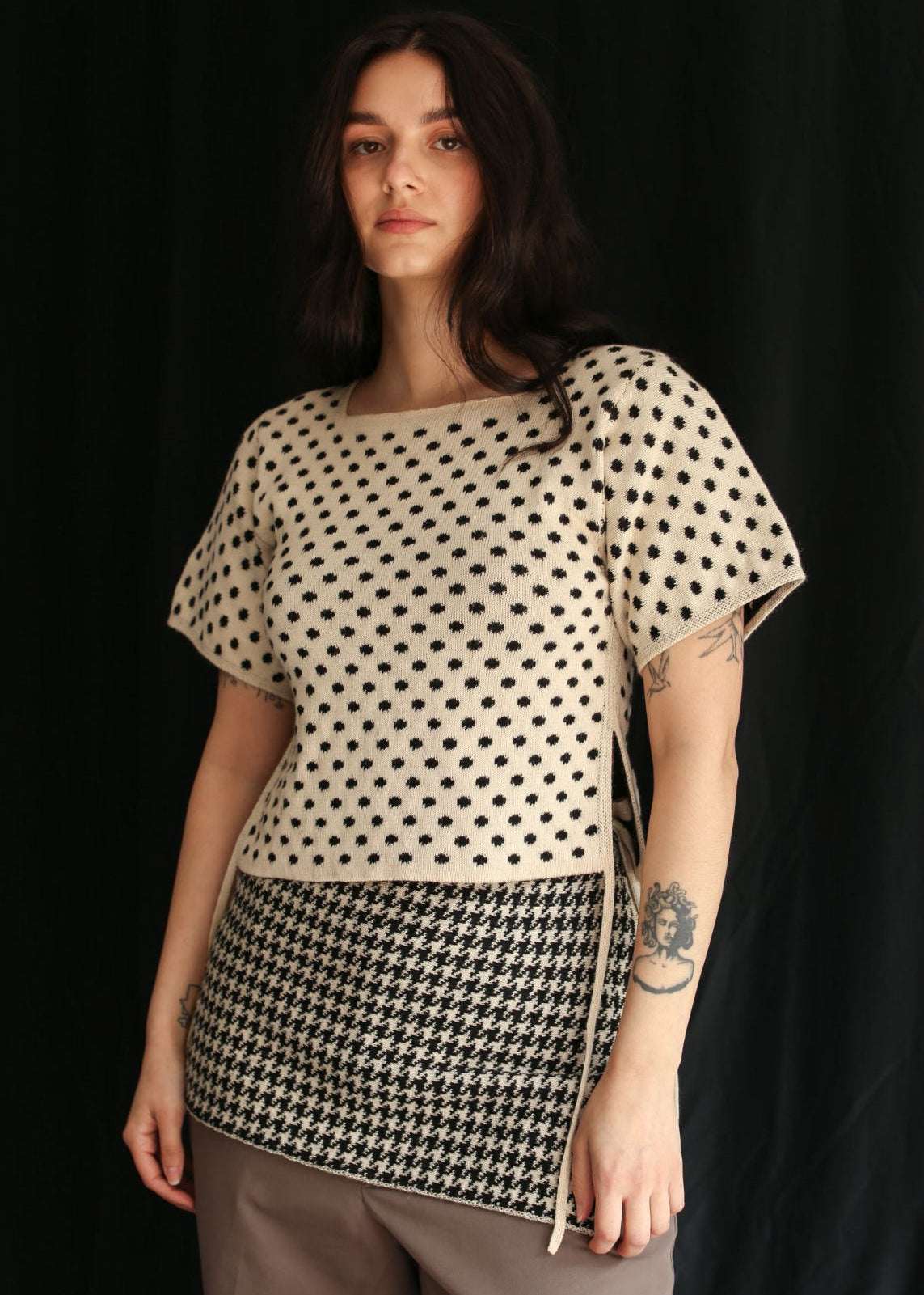 Woman wearing a knitted polka dot top and a houndstooth skirt against a black background