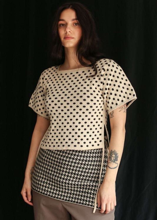 Woman wearing a knitted polka dot top and a houndstooth skirt against a black background