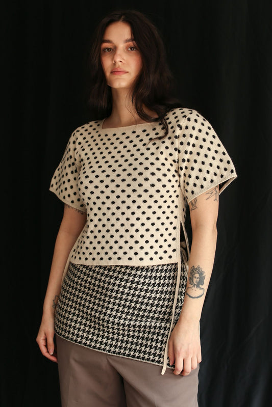Woman wearing a knitted polka dot top and a houndstooth skirt against a black background