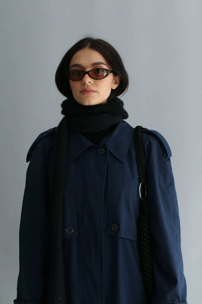 Portrait of a woman wearing a black balaclava and navy trench against a white background