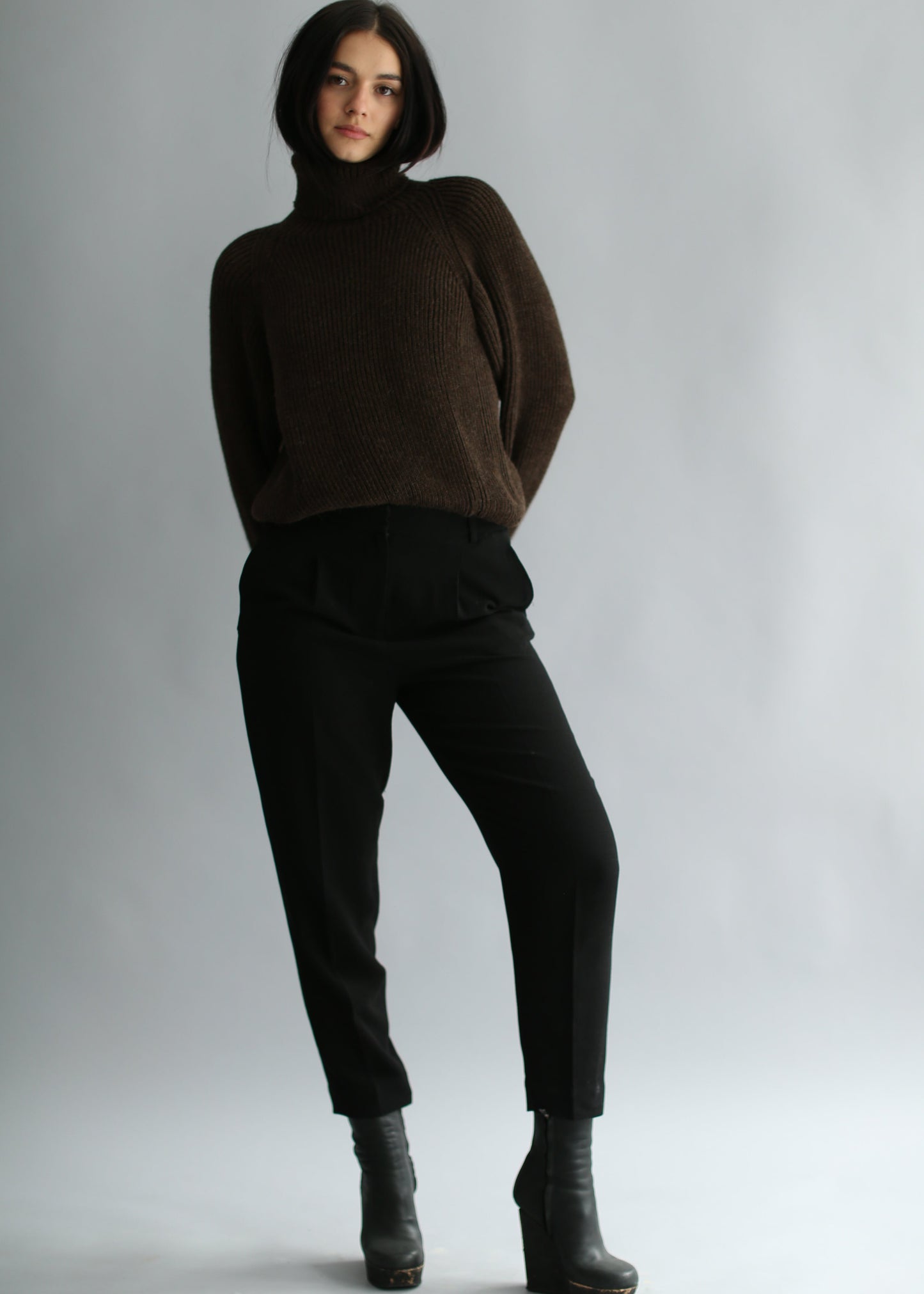 Model wearing a dark brown ribbed sweater and black pants on a plain background