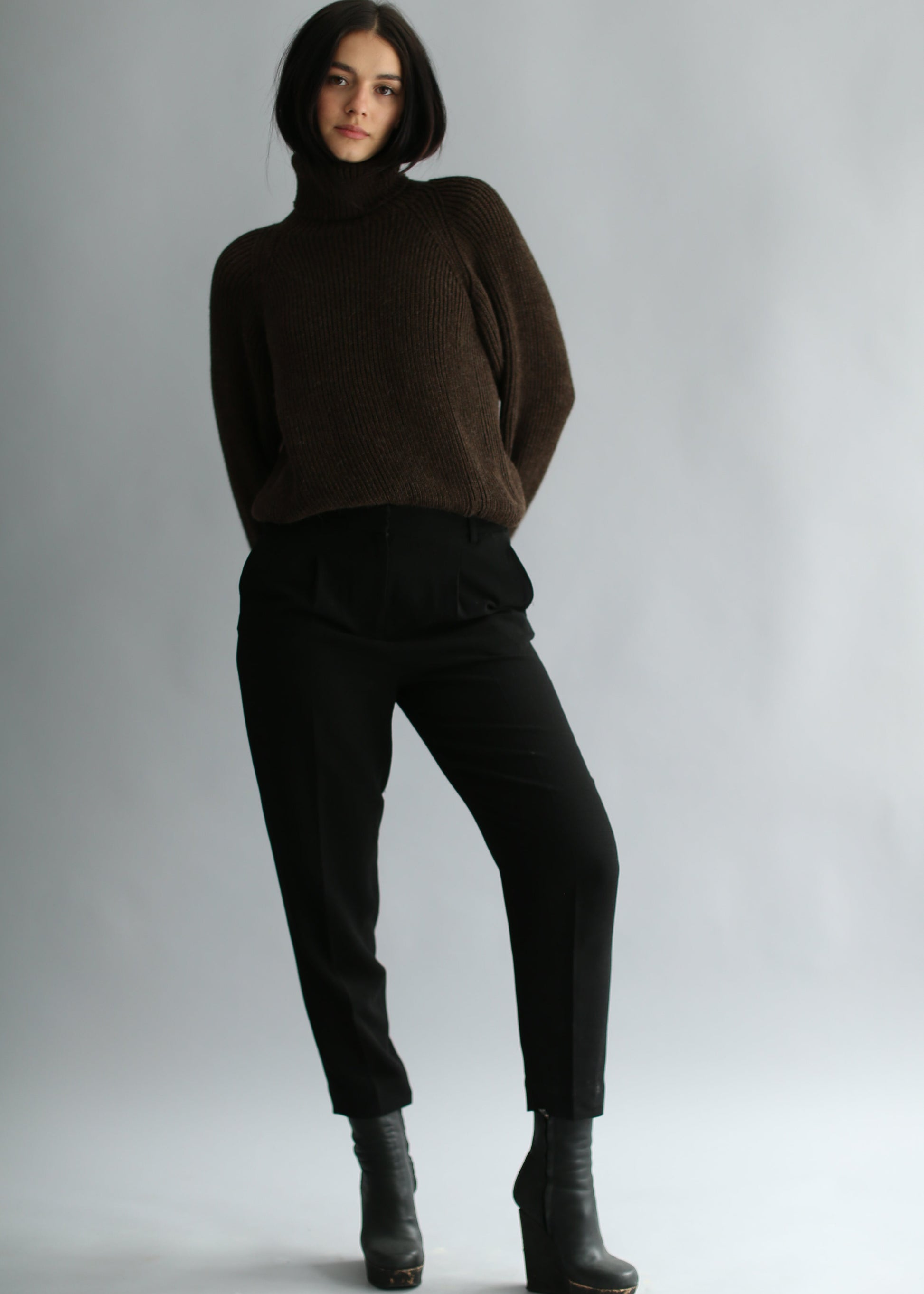Model wearing a dark brown ribbed sweater and black pants on a plain background