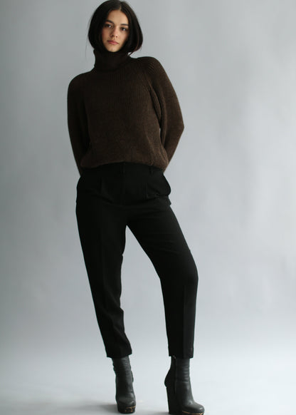 Model wearing a dark brown ribbed sweater and black pants on a plain background