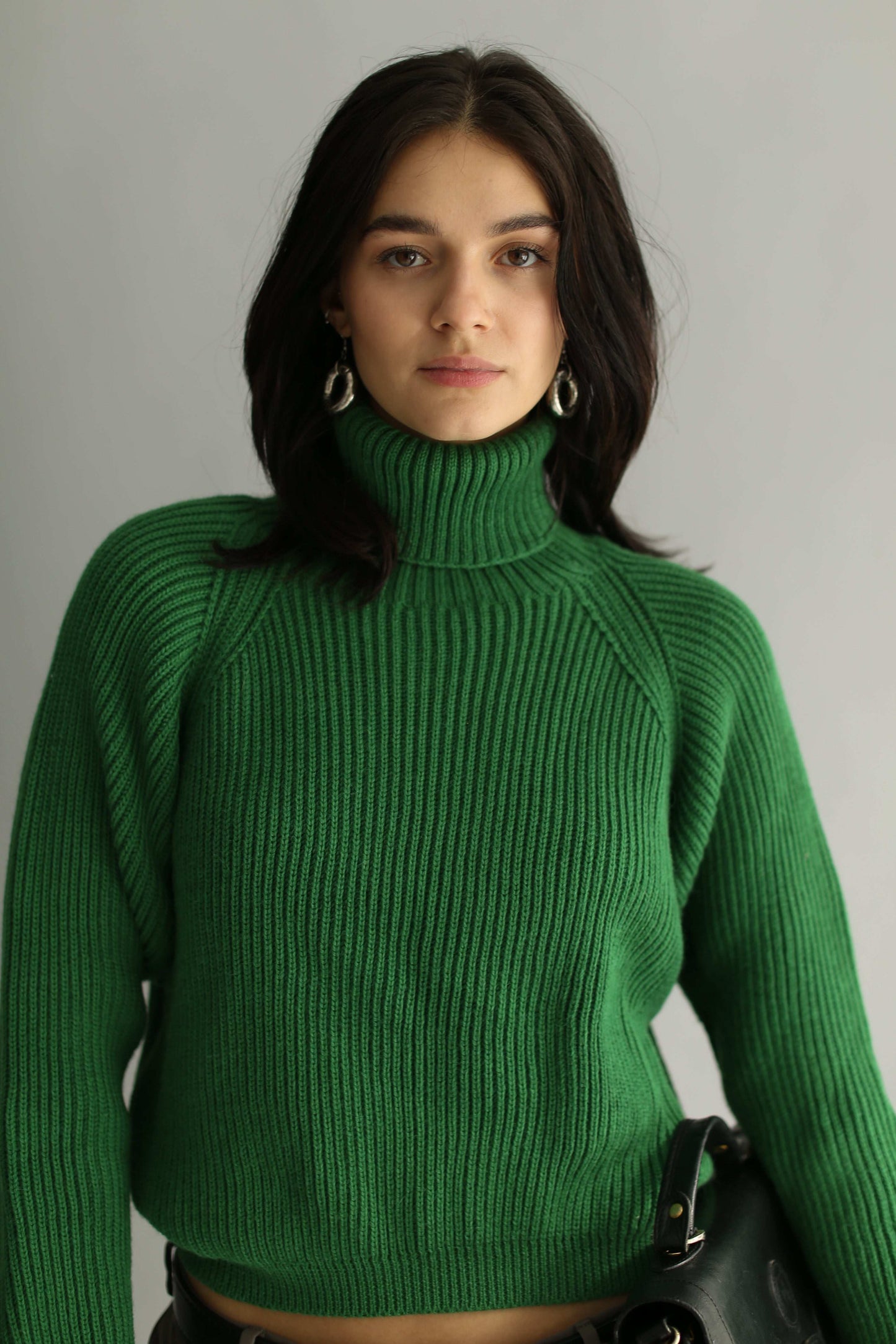 Portrait of a model wearing a green ribbed cropped turtleneck against a white background