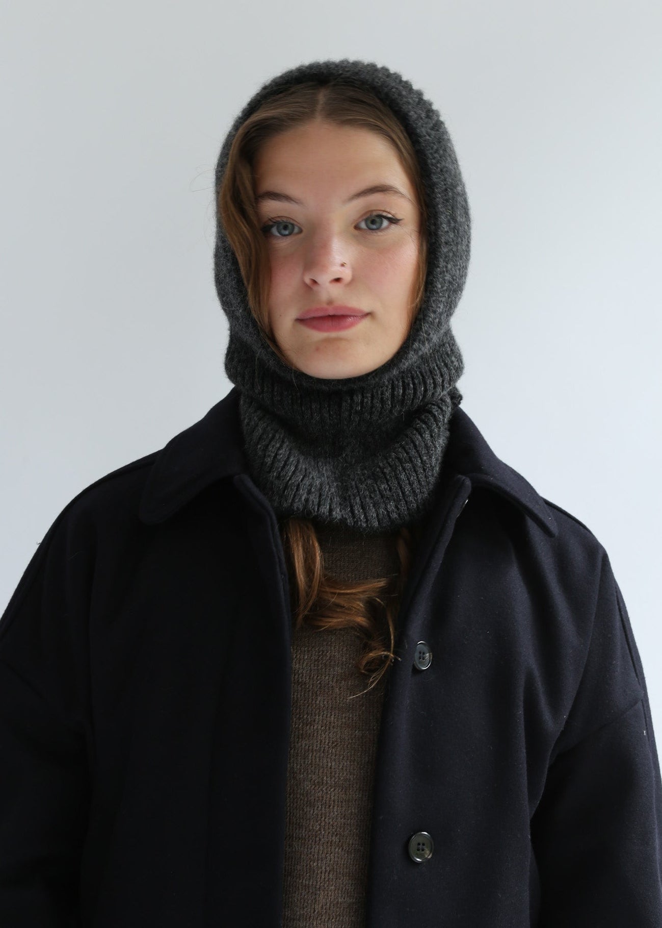 Person wearing a dark coat and gray knitted hood against a plain background