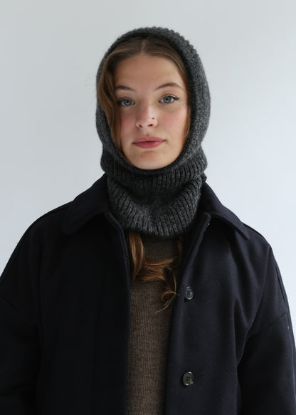 Person wearing a dark coat and gray knitted hood against a plain background