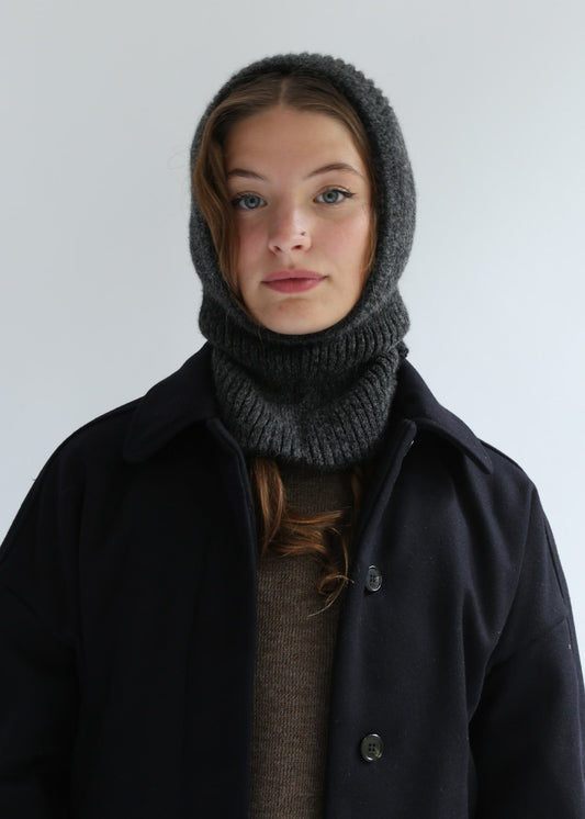 Person wearing a dark coat and gray knitted hood against a plain background