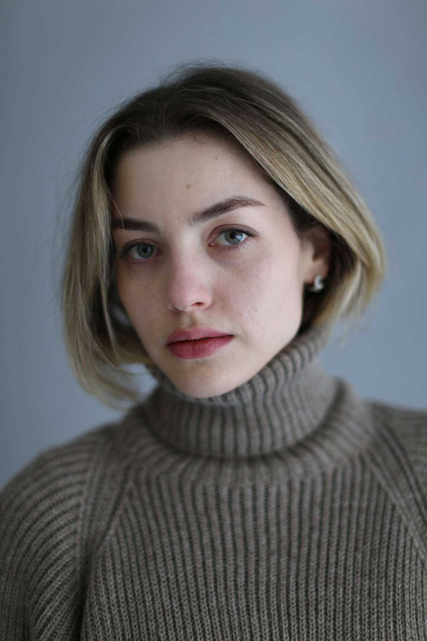 Portait of a model wearing a brown ribbed turtleneck against a white background