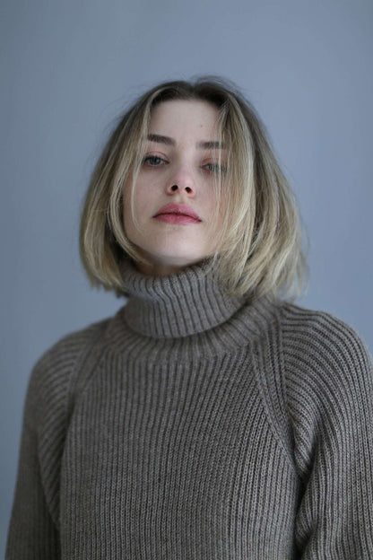 Portait of a blonde model wearing a brown ribbed turtleneck against a white background