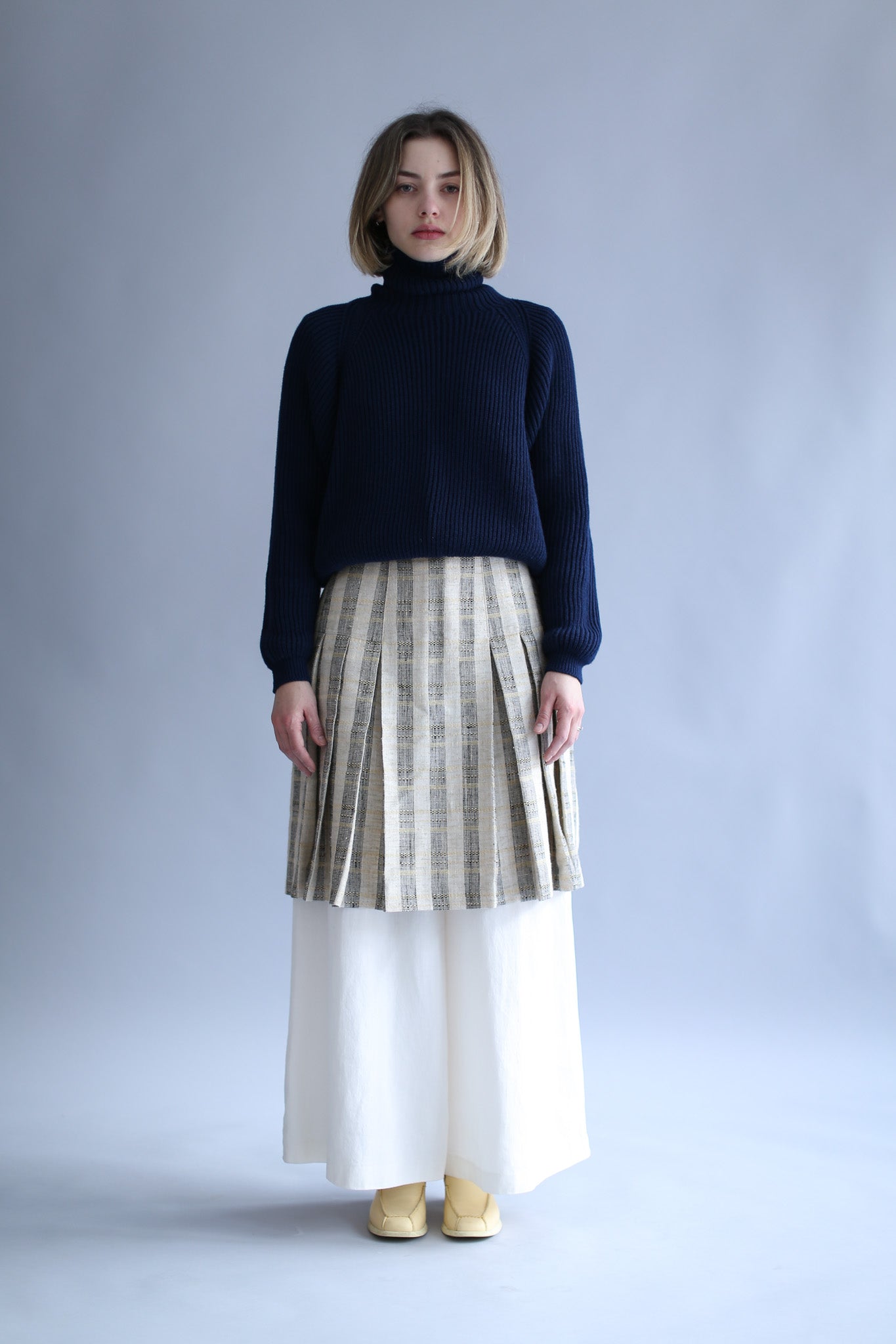Model wearing a navy ribbed turtleneck, stripped long skirt and white wide pants against a white background
