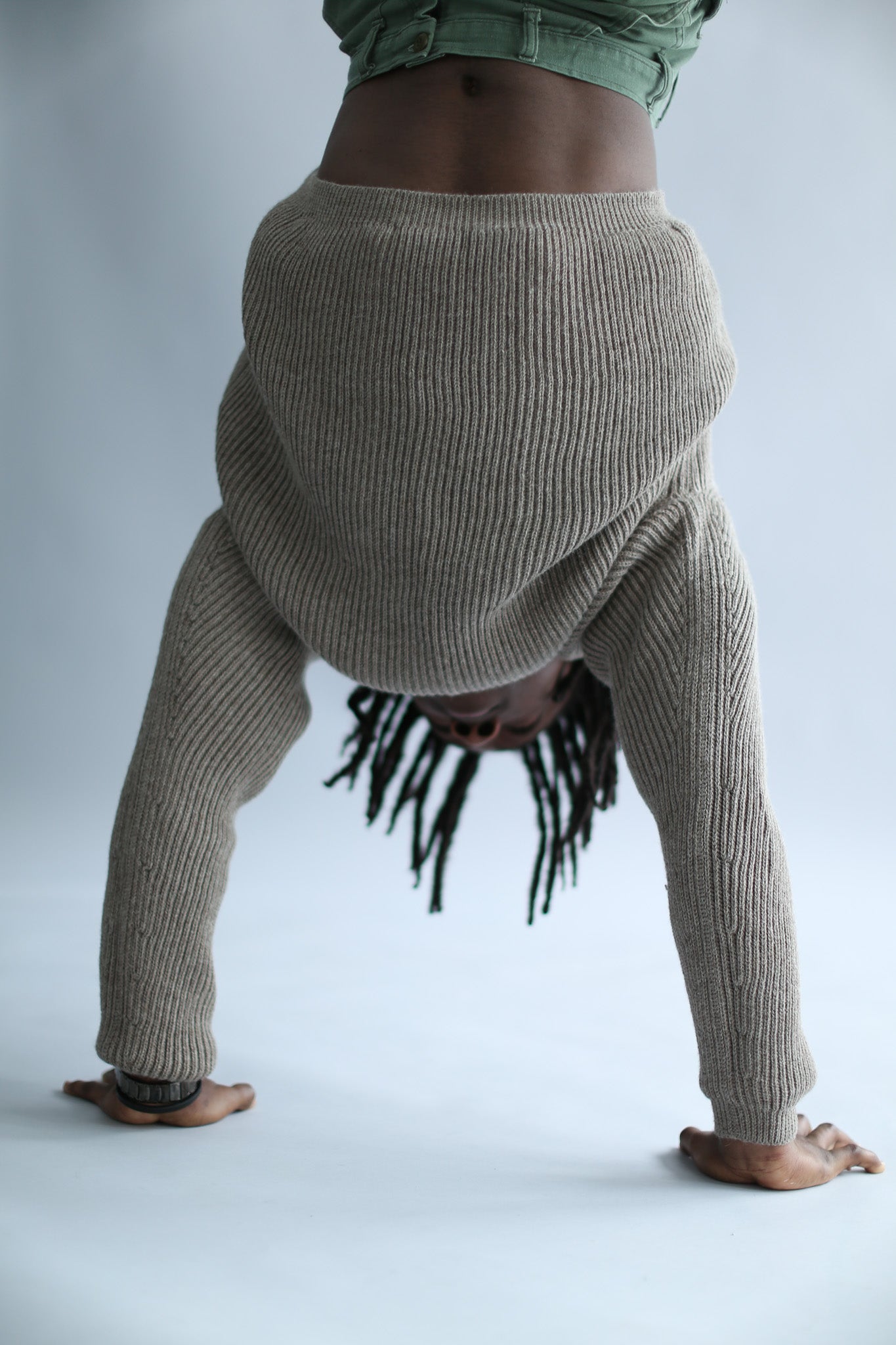 A man walking on his hands wearing a ribbed brown sweater against a white background