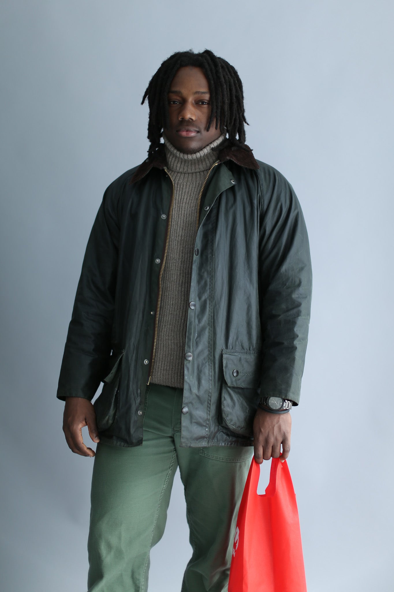 A man wearing a light brown ribbed turtleneck and a waxed jacket against a white background