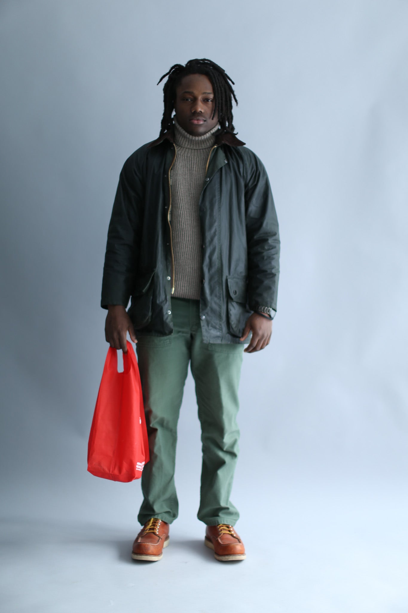 A man wearing a light brown ribbed turtleneck and a waxed jacket against a white background