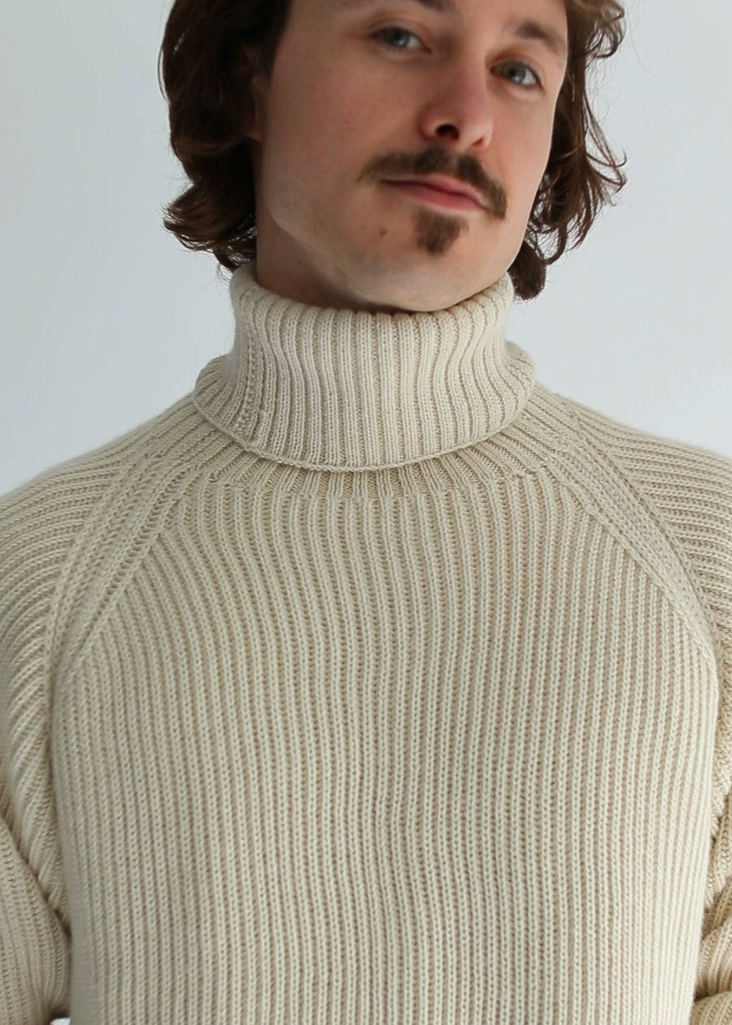 Portrait of a man wearing a white ribbed turtleneck against a white background