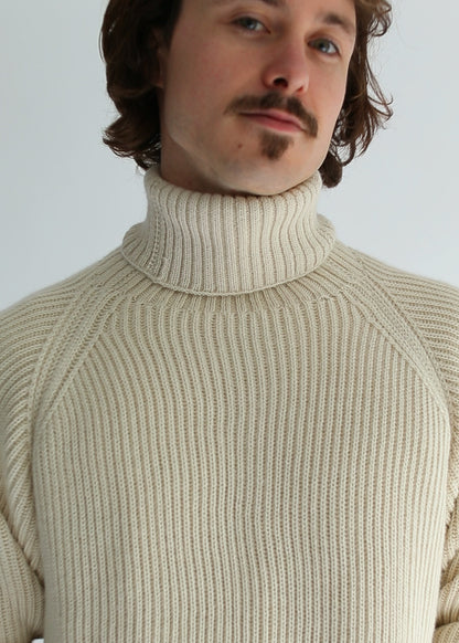 Portrait of a man wearing a white ribbed turtleneck against a white background