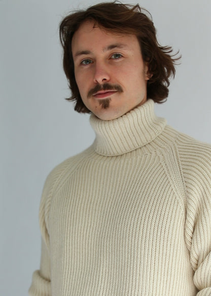 Portrait of a man wearing a light brown ribbed turtleneck against a white background
