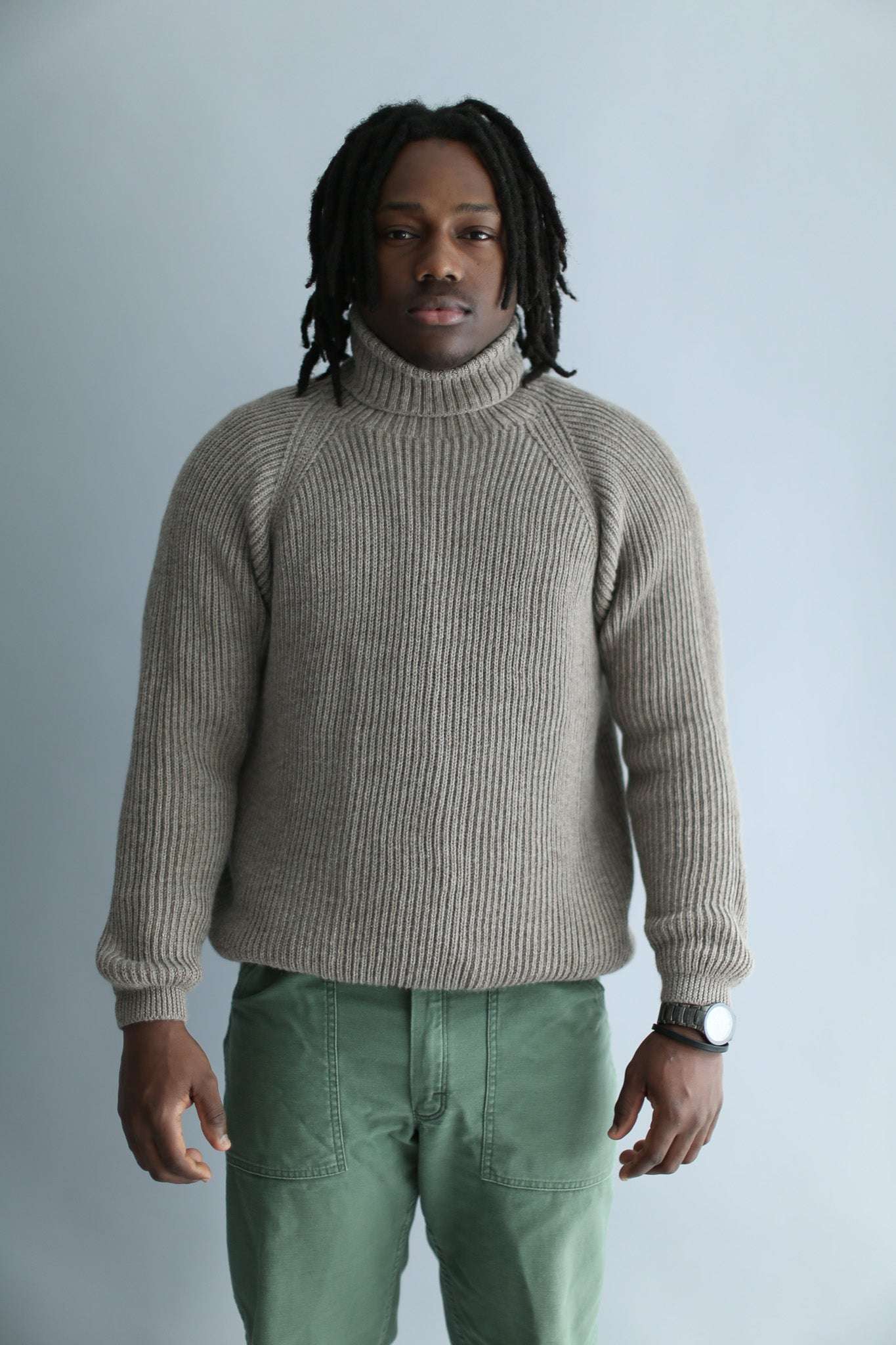 A man wearing a light brown ribbed turtleneck against a white background