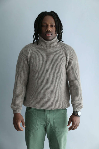 A man wearing a light brown ribbed turtleneck against a white background