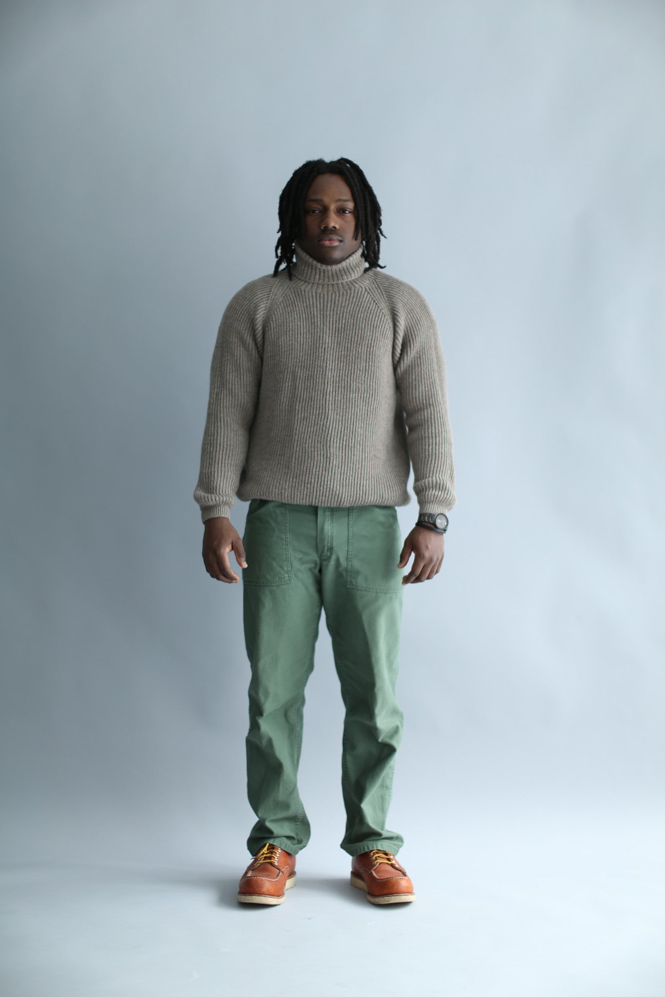 A man wearing a light brown ribbed turtleneck against a white background