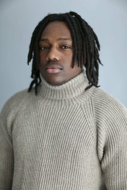 Portrait of a man wearing a light brown ribbed turtleneck against a white background