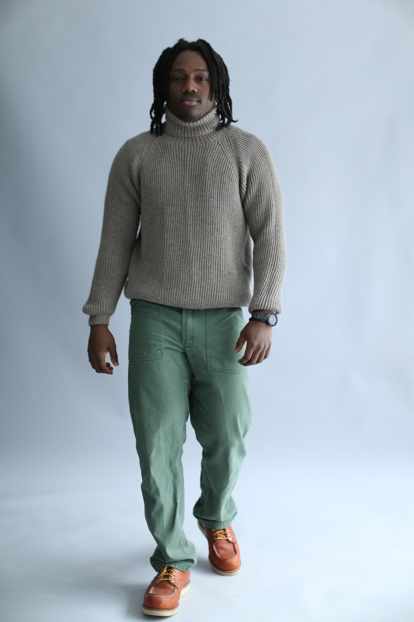 A man wearing a light brown ribbed turtleneck against a white background