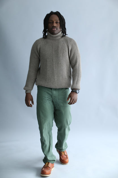 A man wearing a light brown ribbed turtleneck against a white background