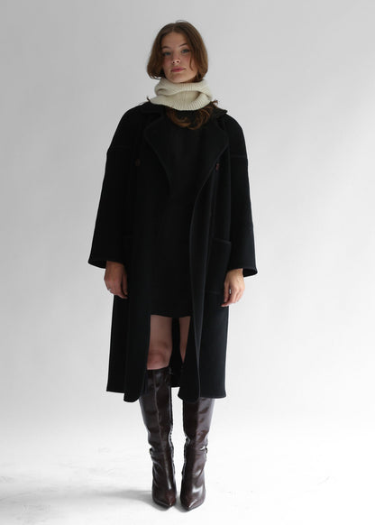 A model wearing a dark coat, skirt, boots and a white balaclava on a white background